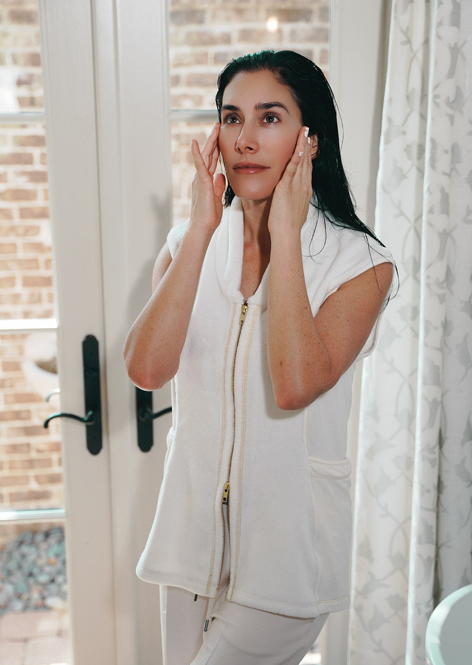 Woman applying skincare product in front of a mirror wearing a post shower vest PSV
