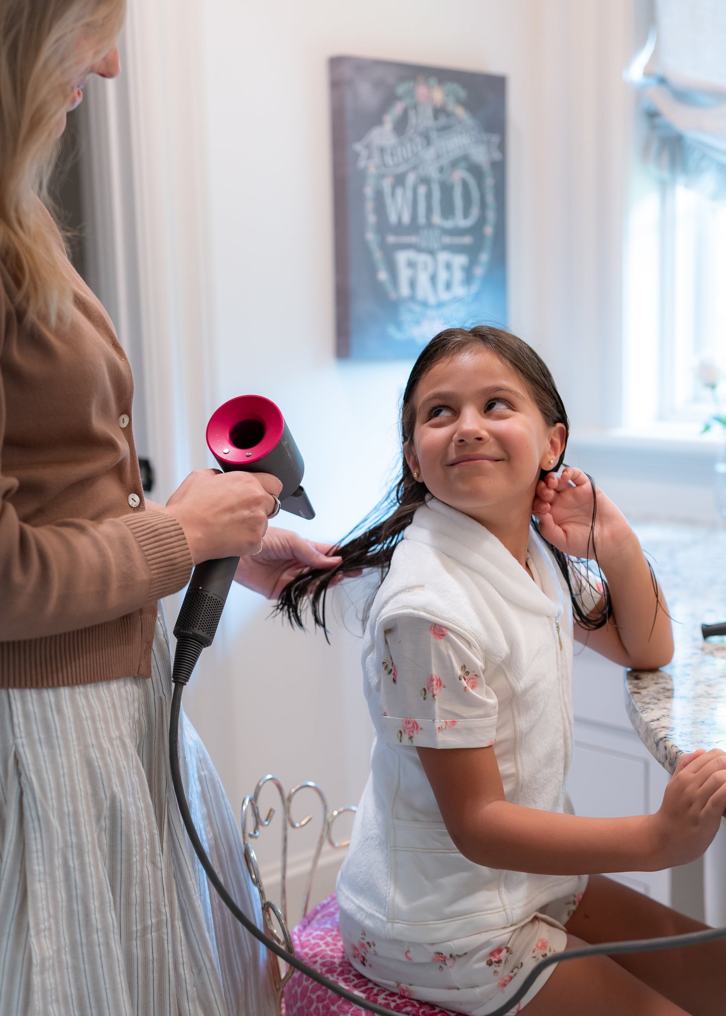 Woman using a hair dryer on a child's hair in a bathroom setting wearing a post shower vest.